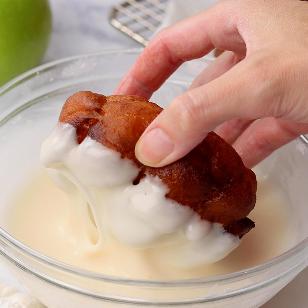 woman's hand dipping Apple Fritters in icing