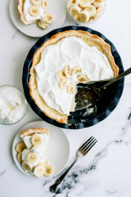 banana cream pie with a slice taken out of it. the slice is on a white plate next to the whole pie