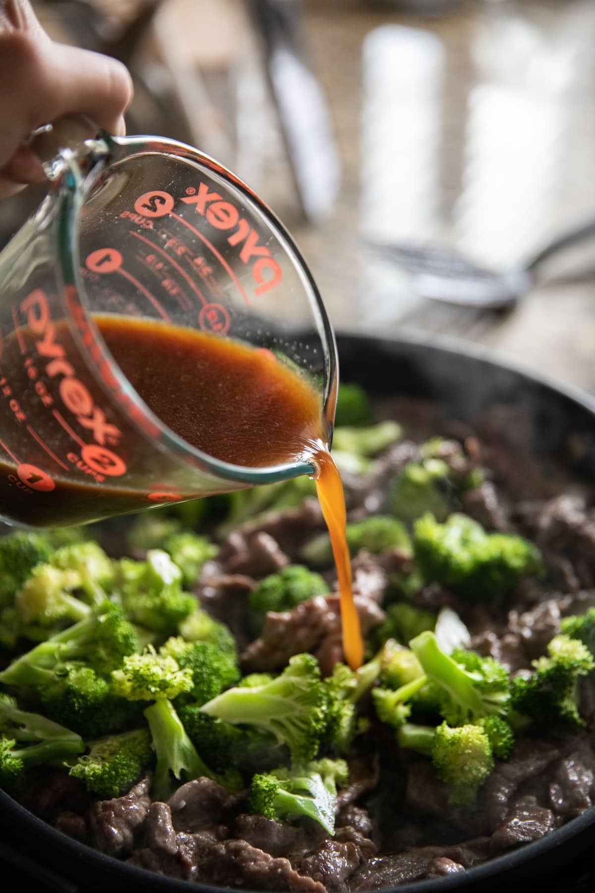 pouring sauce over beef and broccoli in skillet
