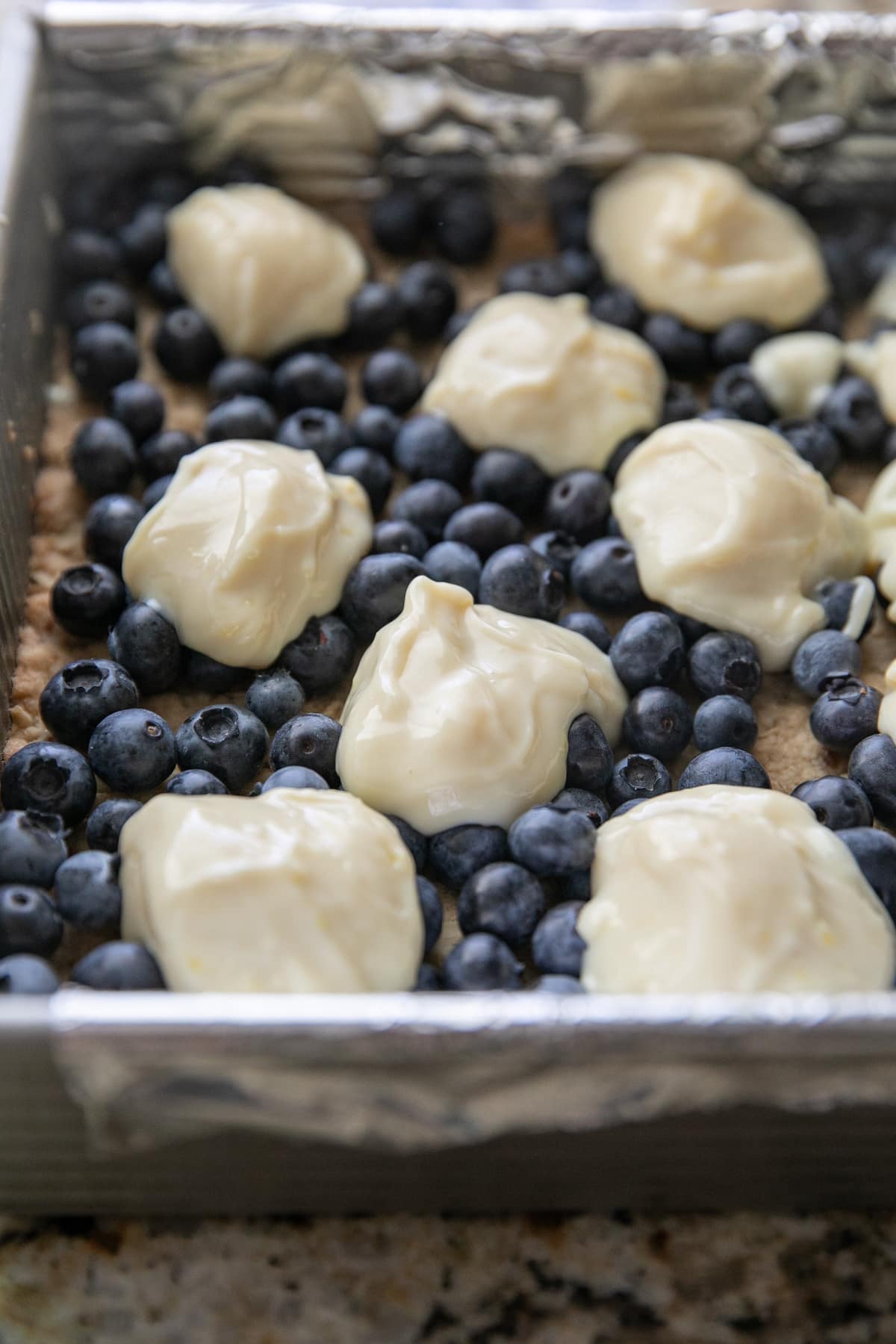 dollops of lemon mixture topping blueberries in a baking pan