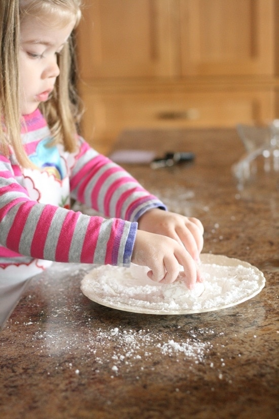 girl rolling cookie dough in powdered sugar