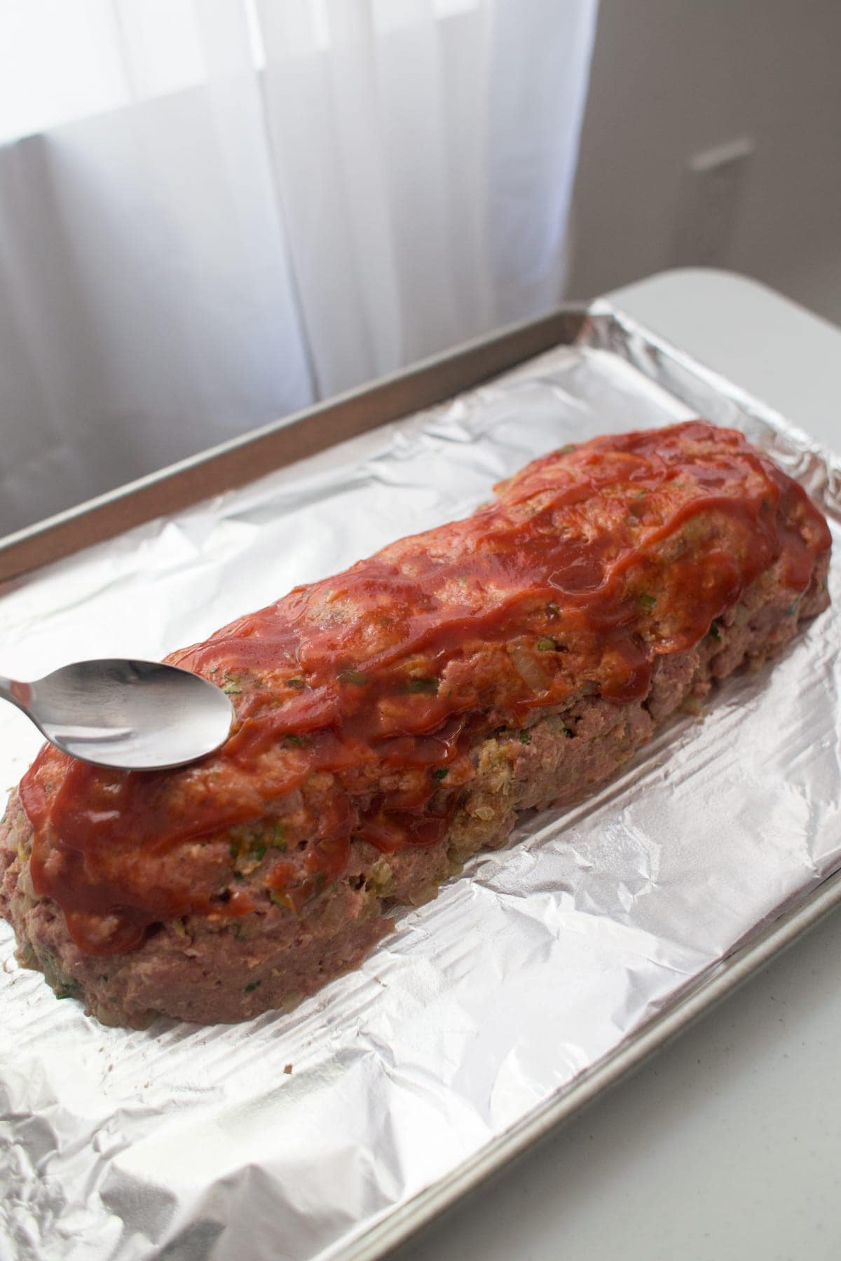 raw meatloaf on a tinfoil lined baking sheet being glazes with ketchup
