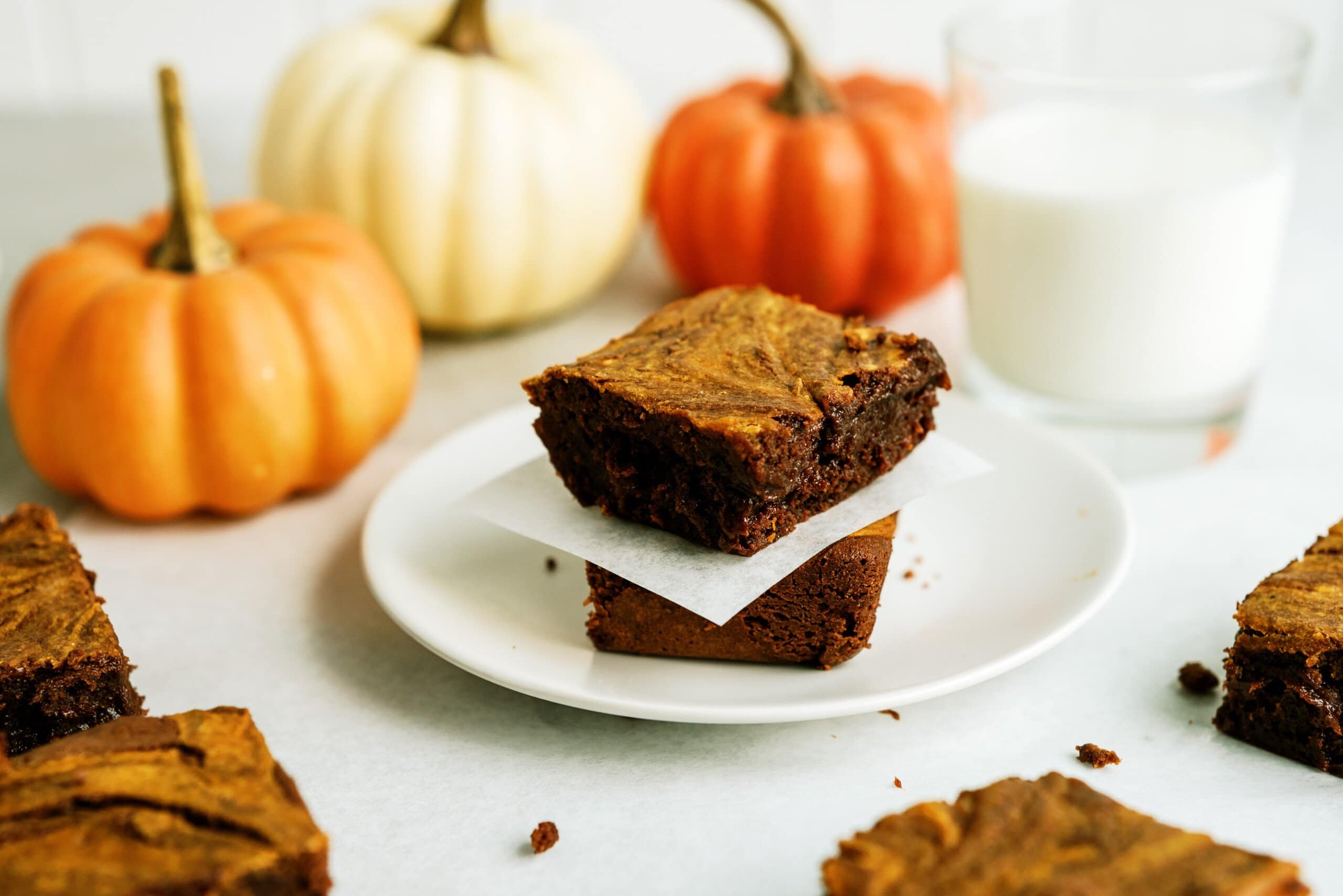 two pumpkin brownies stacked on top of each other separated by parchment paper all on a white plate