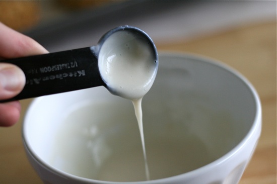 Greek Yogurt glaze being poured out of a measuring spoon into a bowl