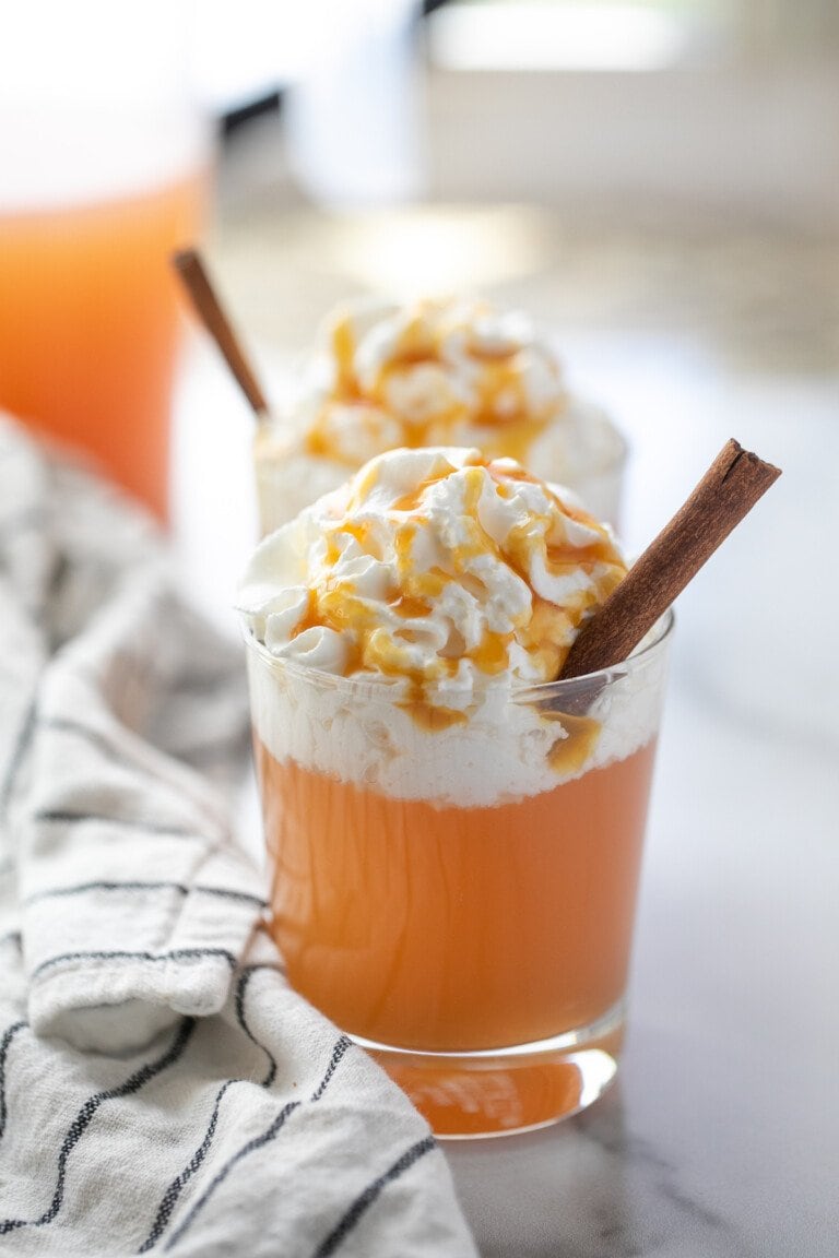 apple cider in a glass cup topped with whipped cream and a cinnamon stick