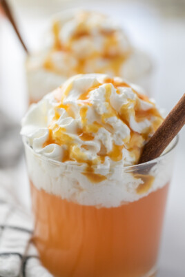 close up of apple cider in a glass topped with whipped cream and a cinnamon stick