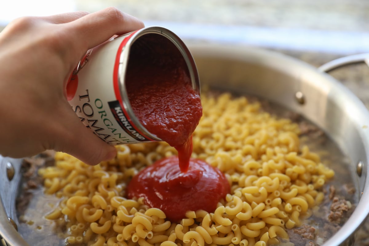 pouring tomato sauce into pan over macaroni