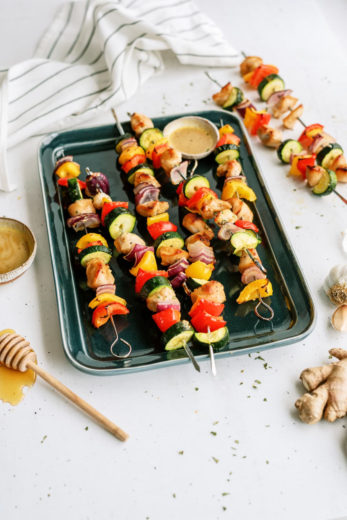 honey-soy-chicken-kabobs on oval white background on green tray with bowl of sauce