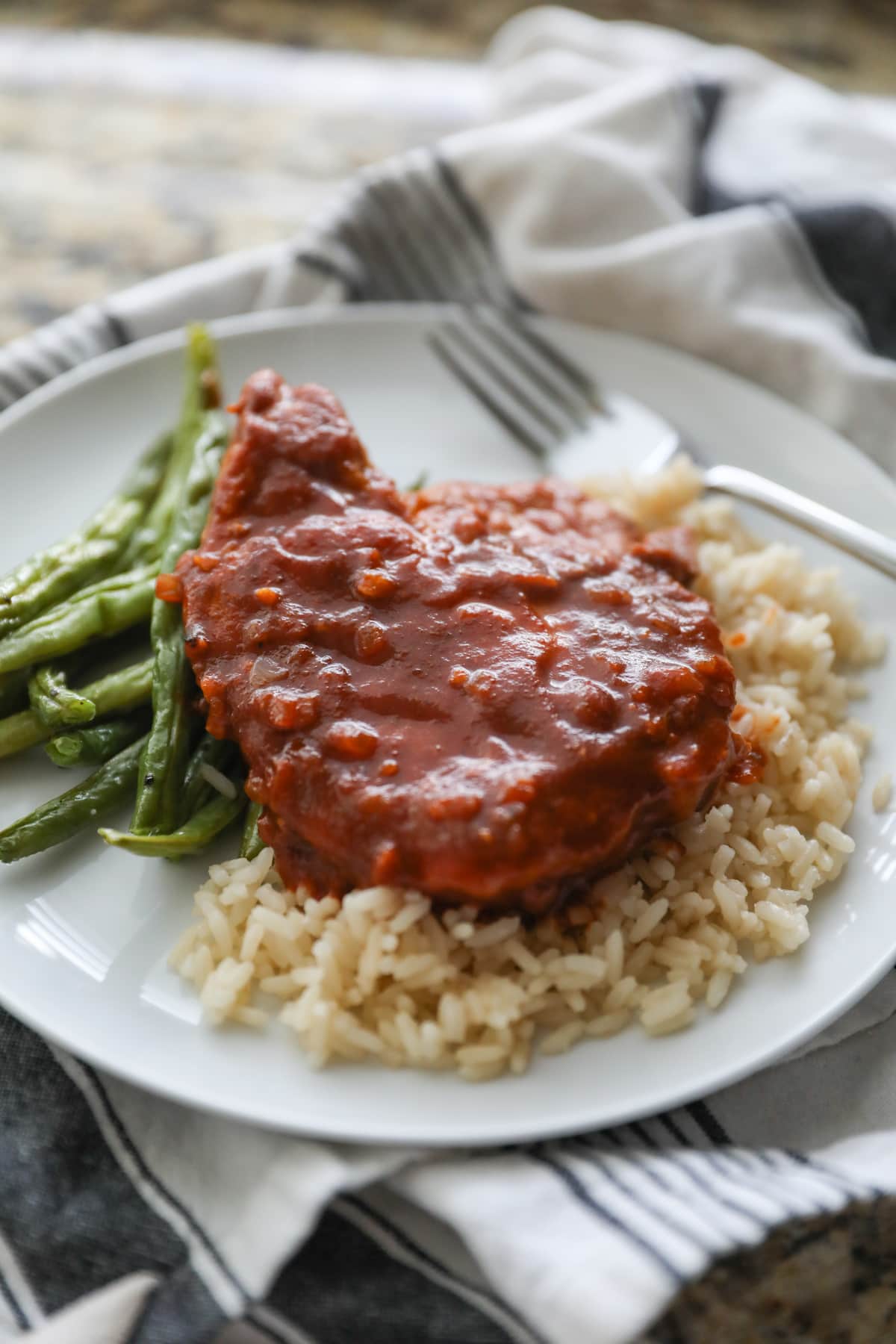 pork chop on white plate with rice and green beans