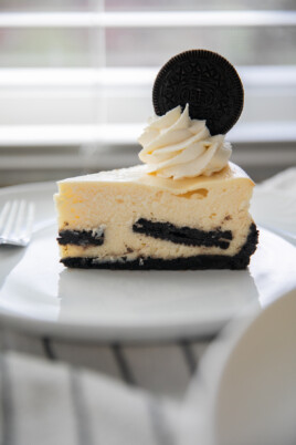 a slice of oreo cheesecake topped with whipped cream and an oreo cookie all on a white plate