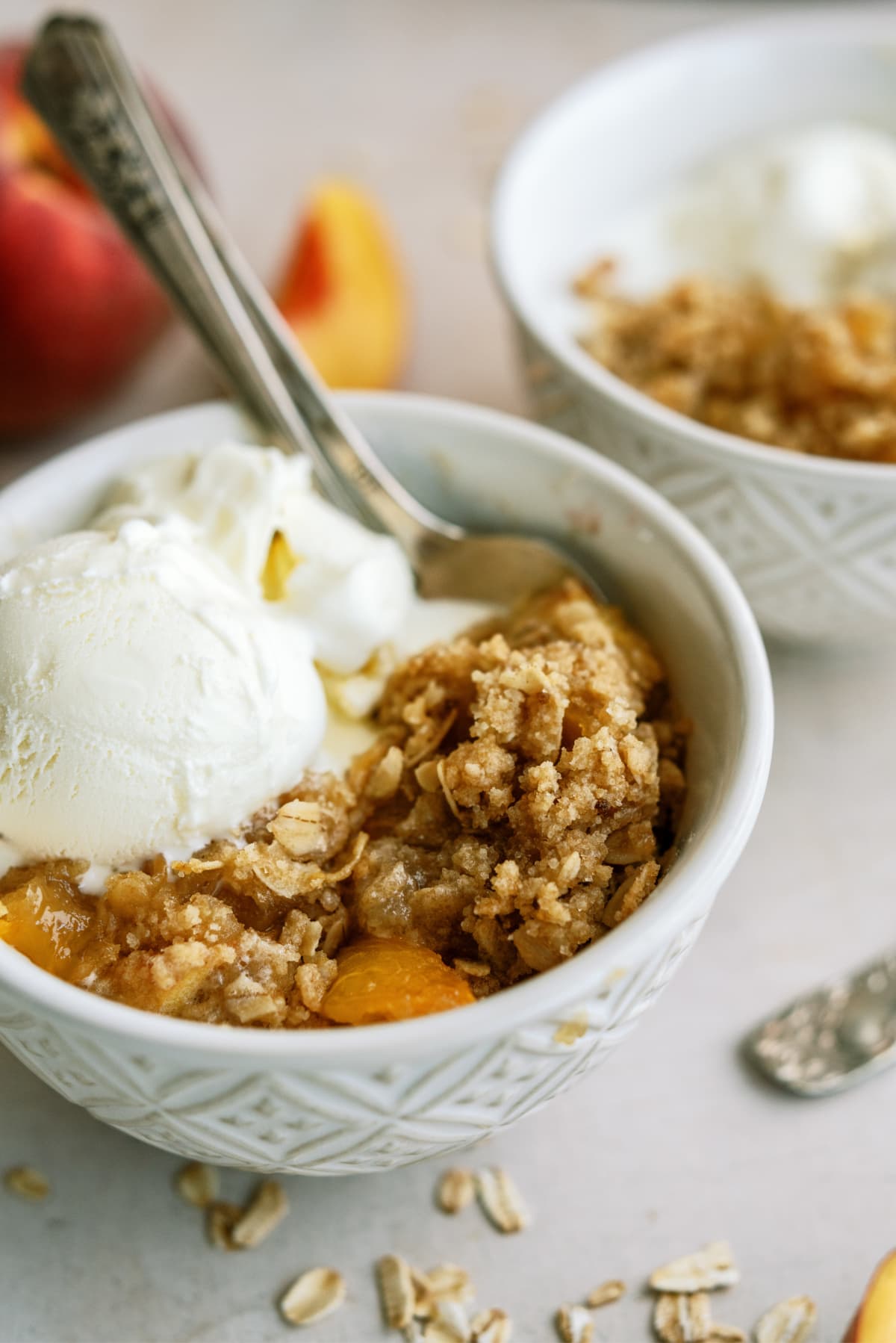 peach-crisp in bowl with spoon and ice cream