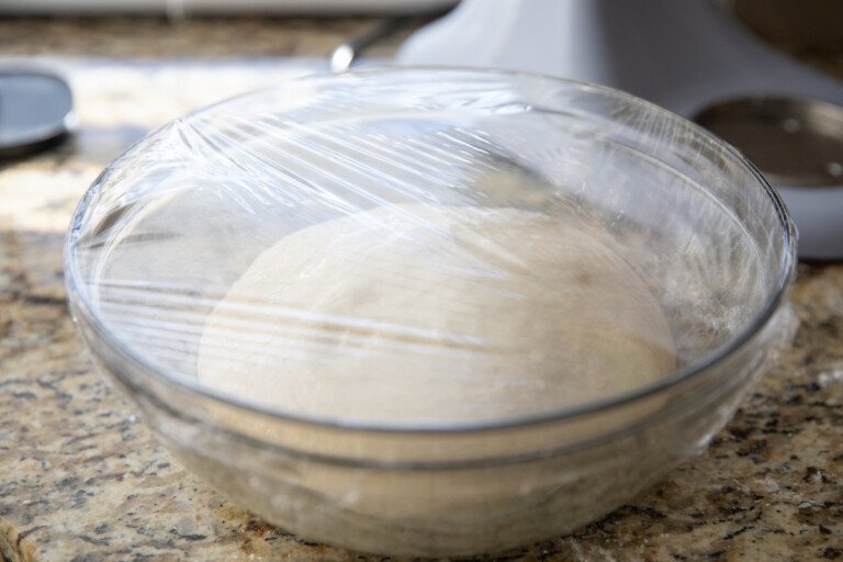 pizza dough in bowl covered with plastic wrap