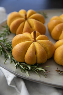 pumpkin bread rolls on a serving plate with greenery