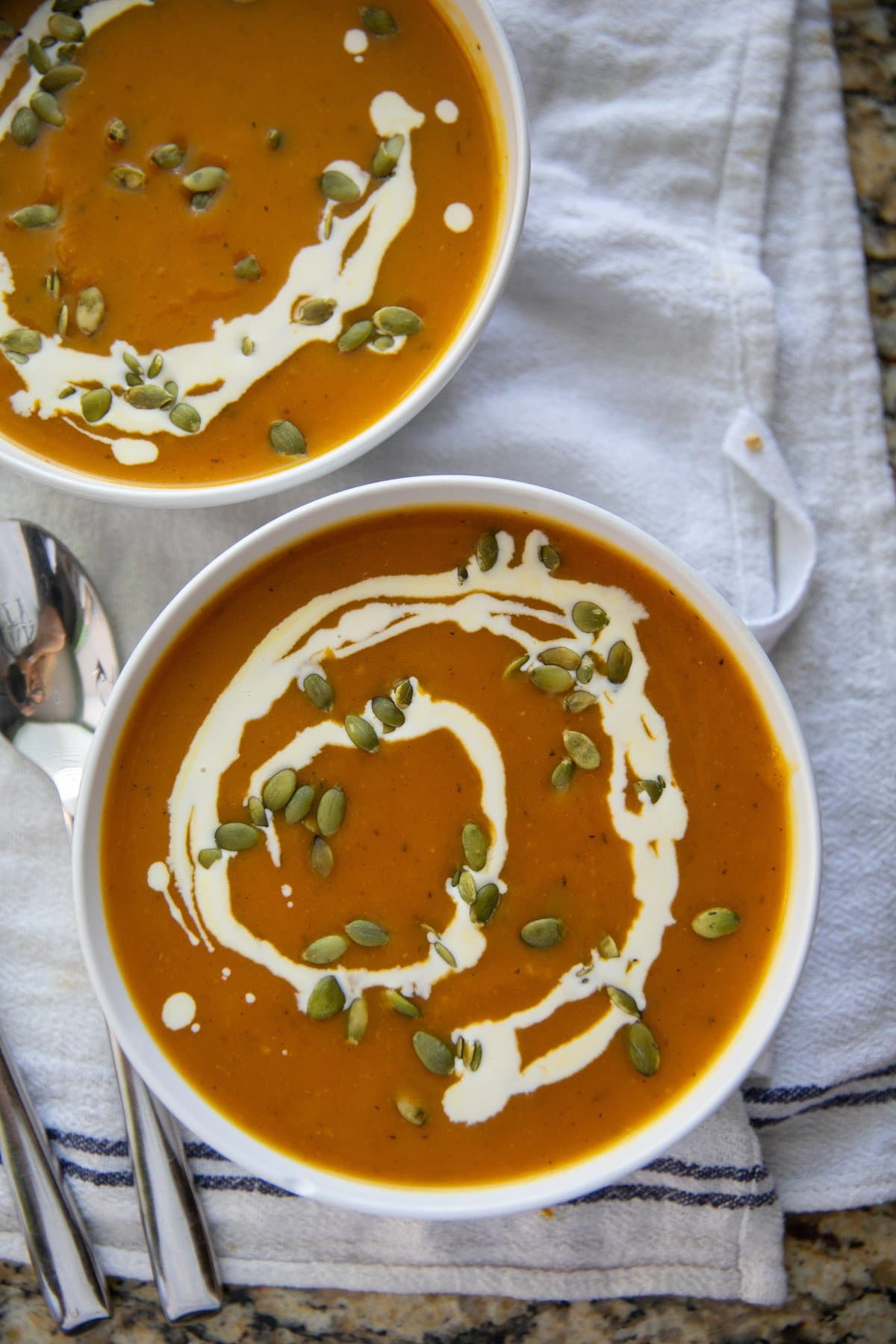 top down view of pumpkin soup in two bowls with a swirl of cream and topped with pepitas