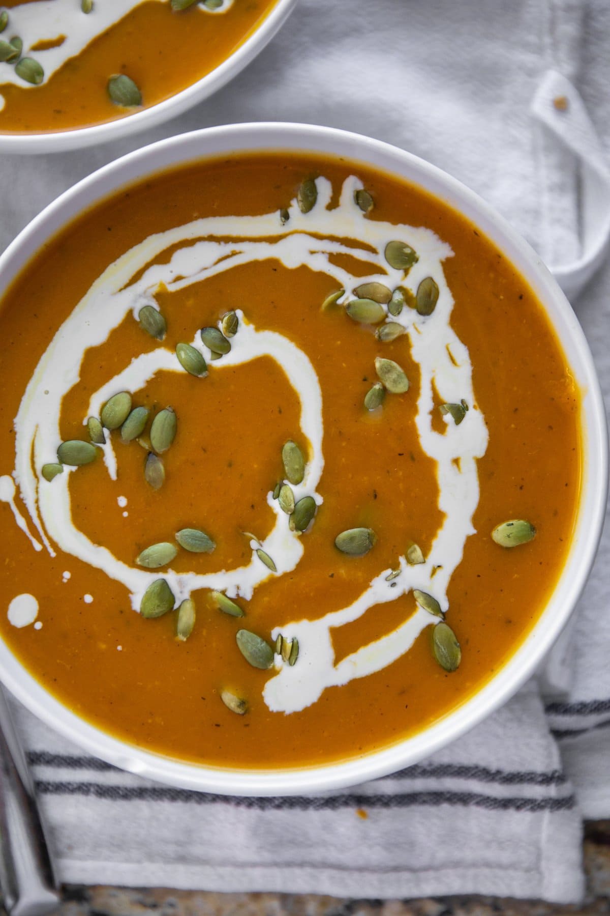 pumpkin soup in a bowl with a cream swirl and topped with pepitas