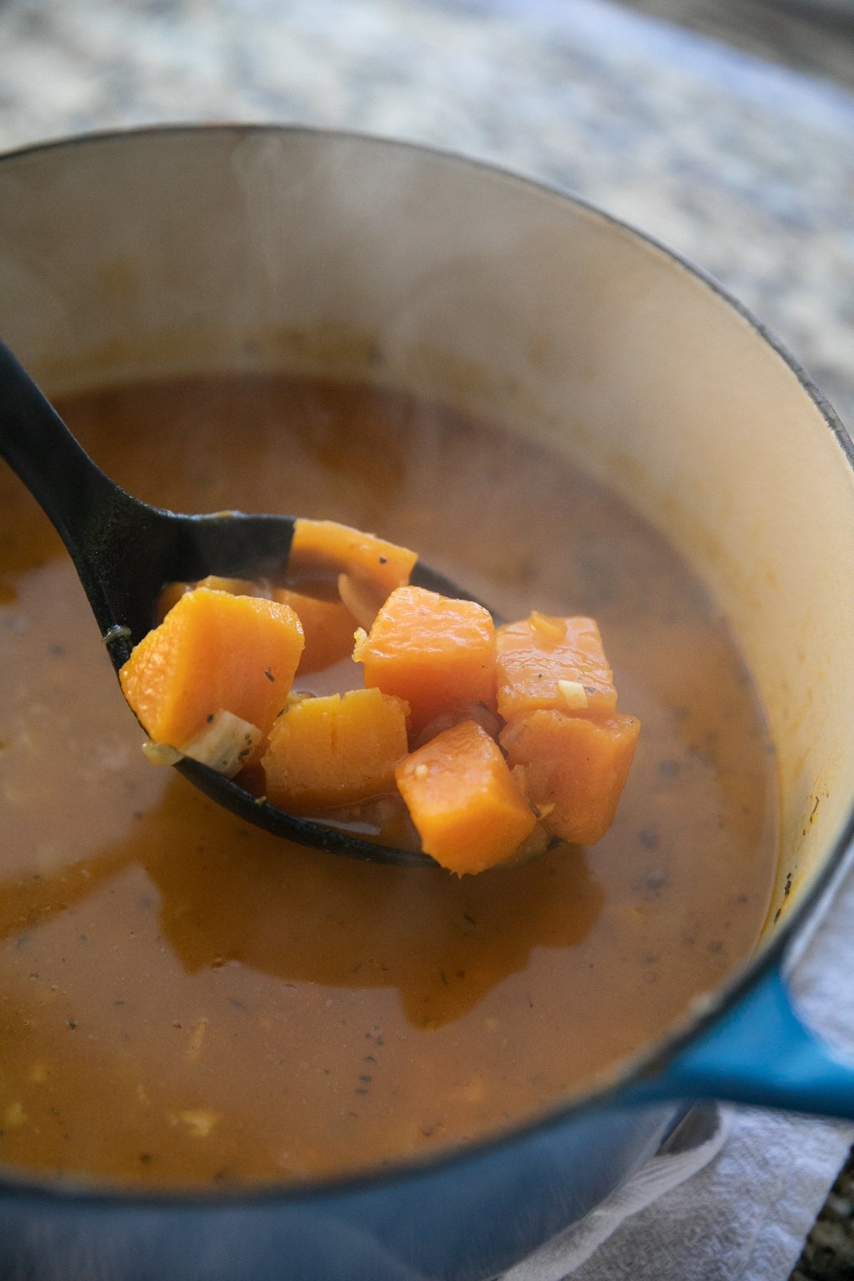 scooping pumpkin into soup base all in a pot