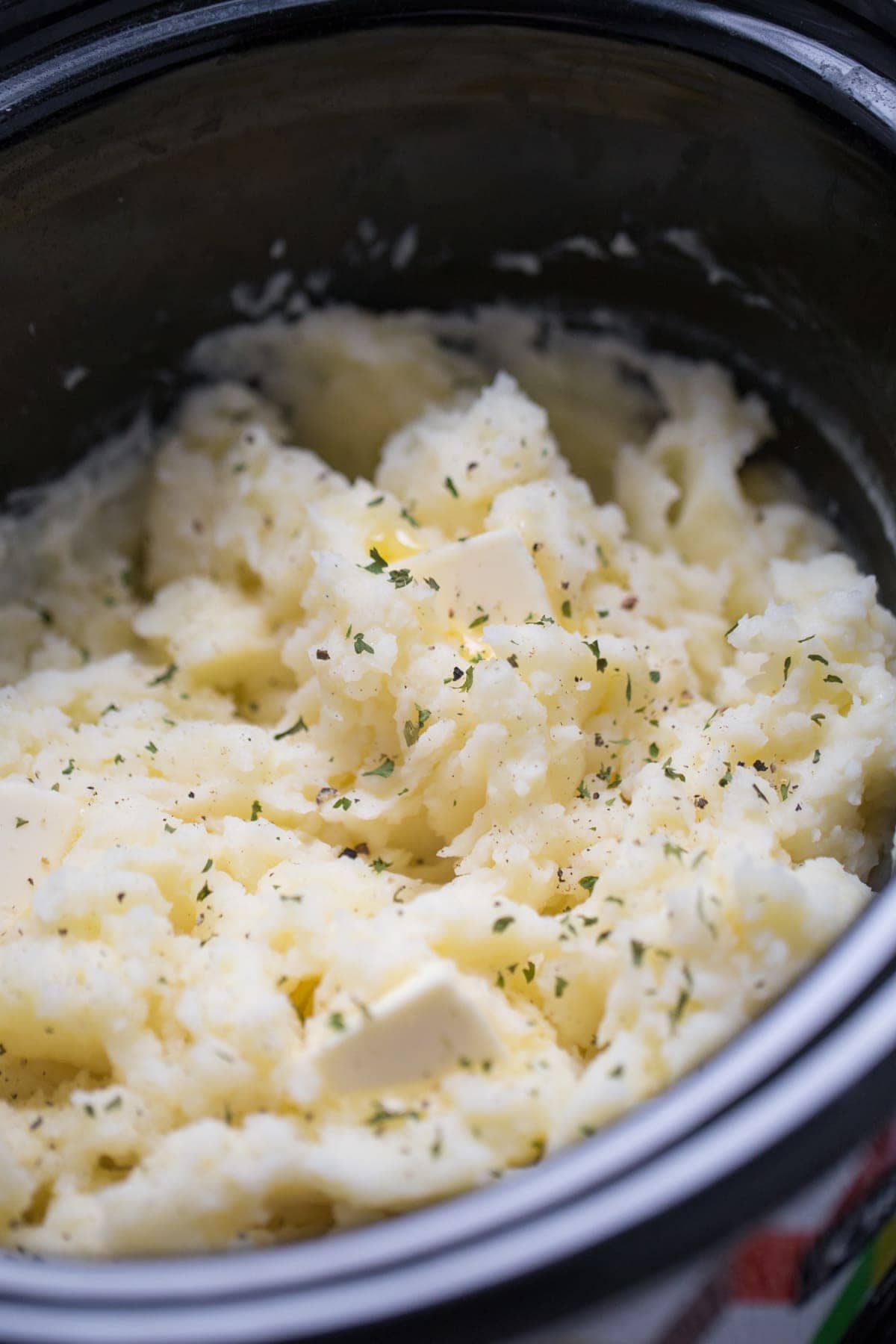 mashed potatoes in a crockpot with slices of melted butter and garnish