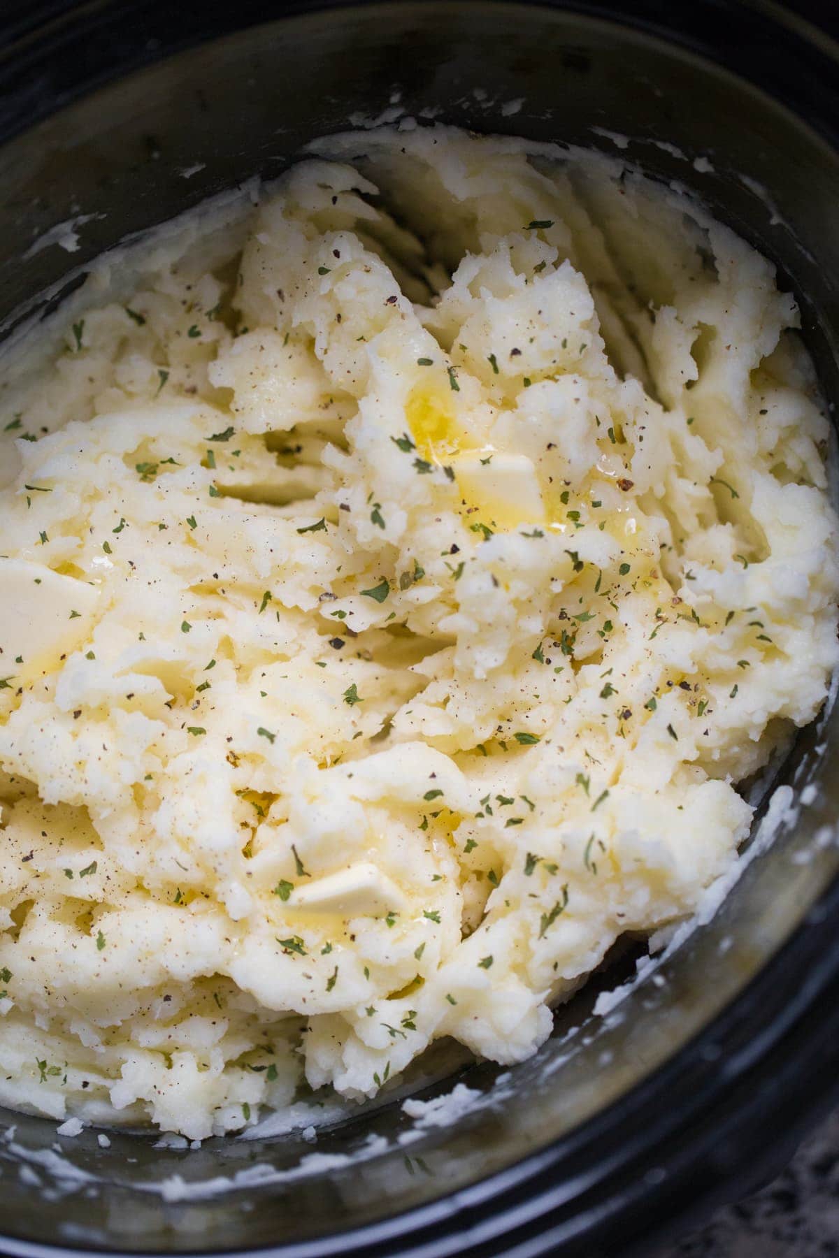 mashed potatoes in a crockpot with slices of melted butter and garnish
