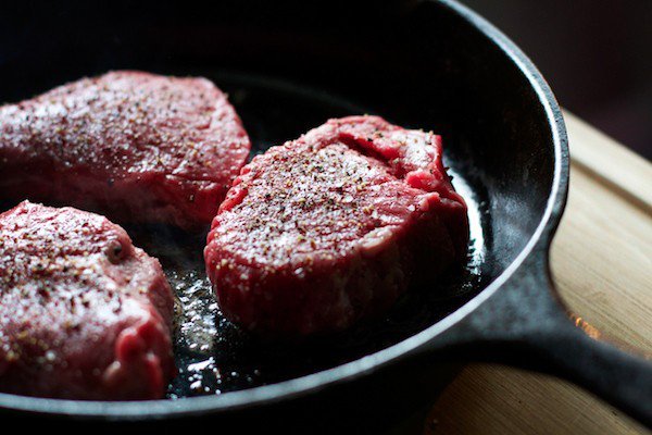 raw steaks cooking in pan with salt and pepper