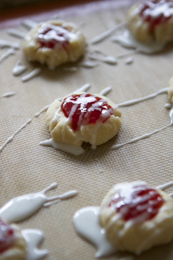 vanilla shortbread thumbprint cookies filled with jam and topped with icing all on a baking sheet